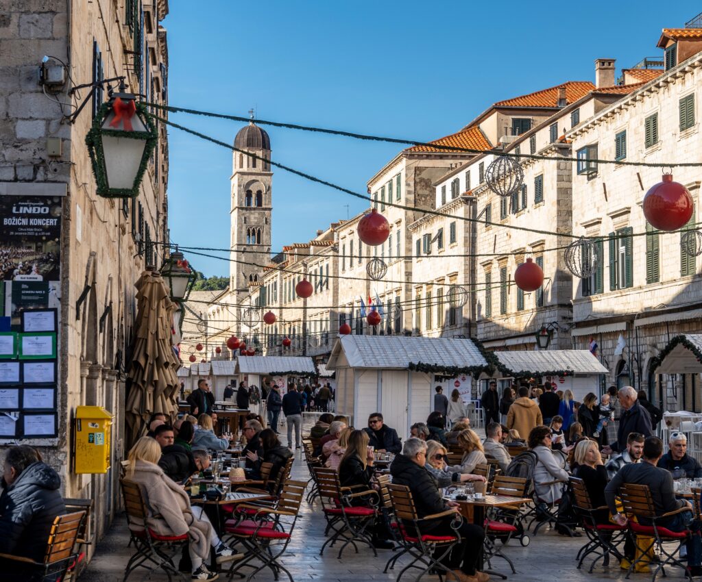 Dubrovnik Christmas Market with decorations overhead as people sit, talk, eat and drink from the Christmas market stalls lining the streets