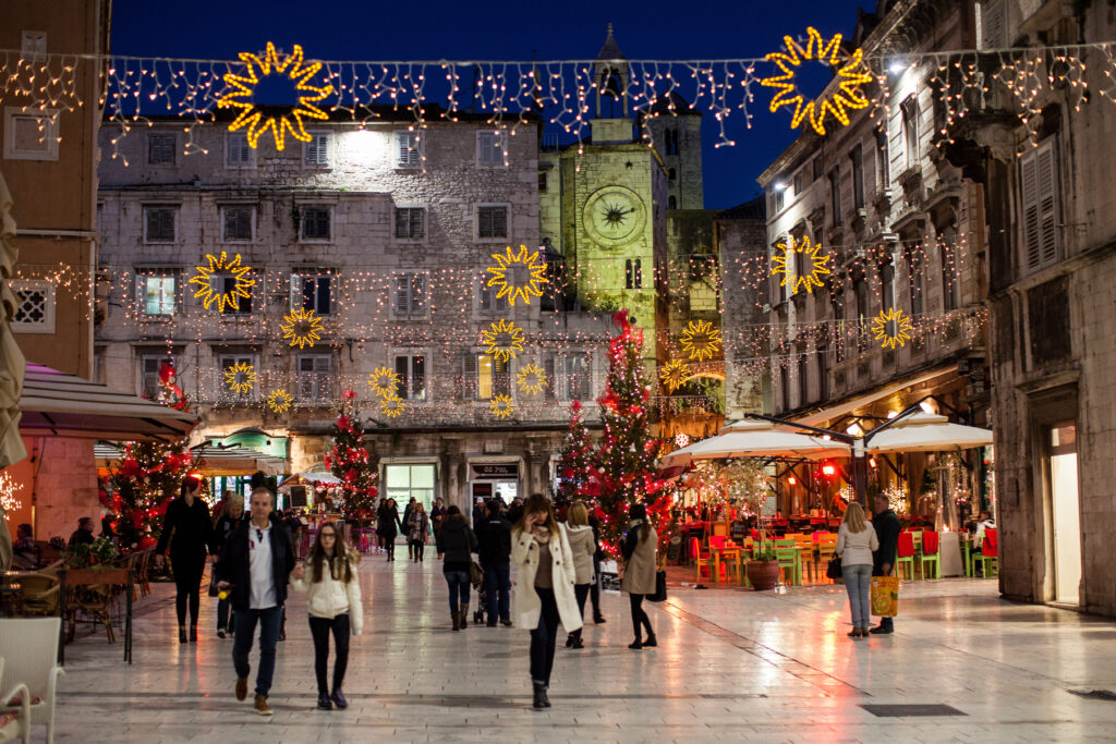 Split Christmas Market with lit up decorations overhead and people walk the old town streets at night