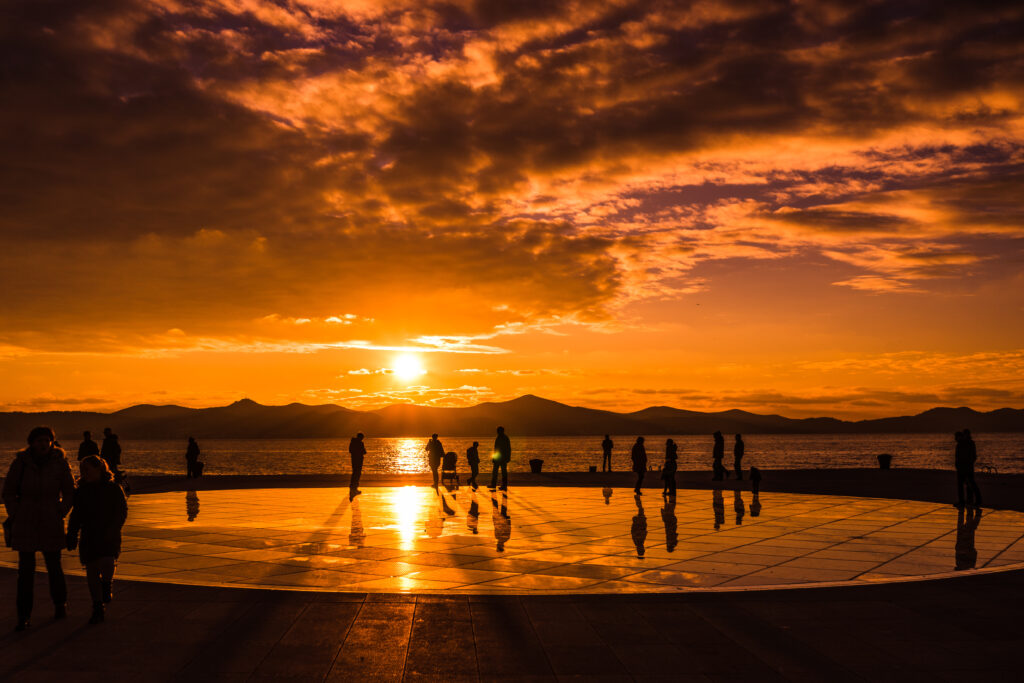 Croatia sunset in Zadar over the Greeting to the Sun monument as people wander around talking