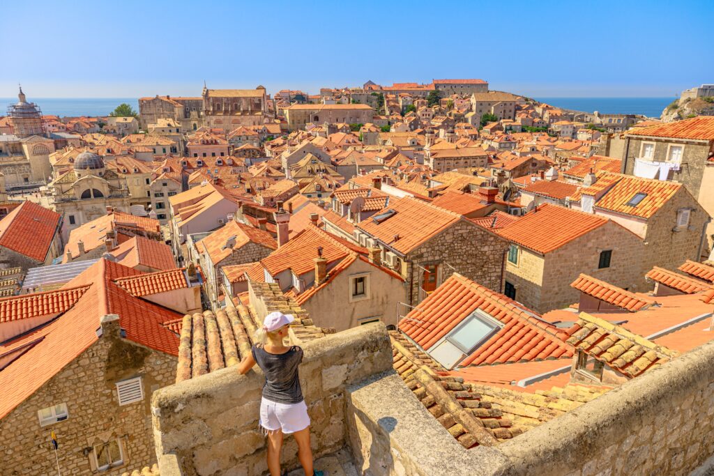 solo travelers looking standing on a concrete balcony overlooking the terracotta rooftops in the Old Town in Dubrovnik 