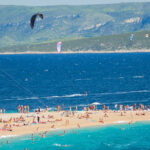 Brač Island beach with people swimming, sunbathing and flying with parachutes high in the sky