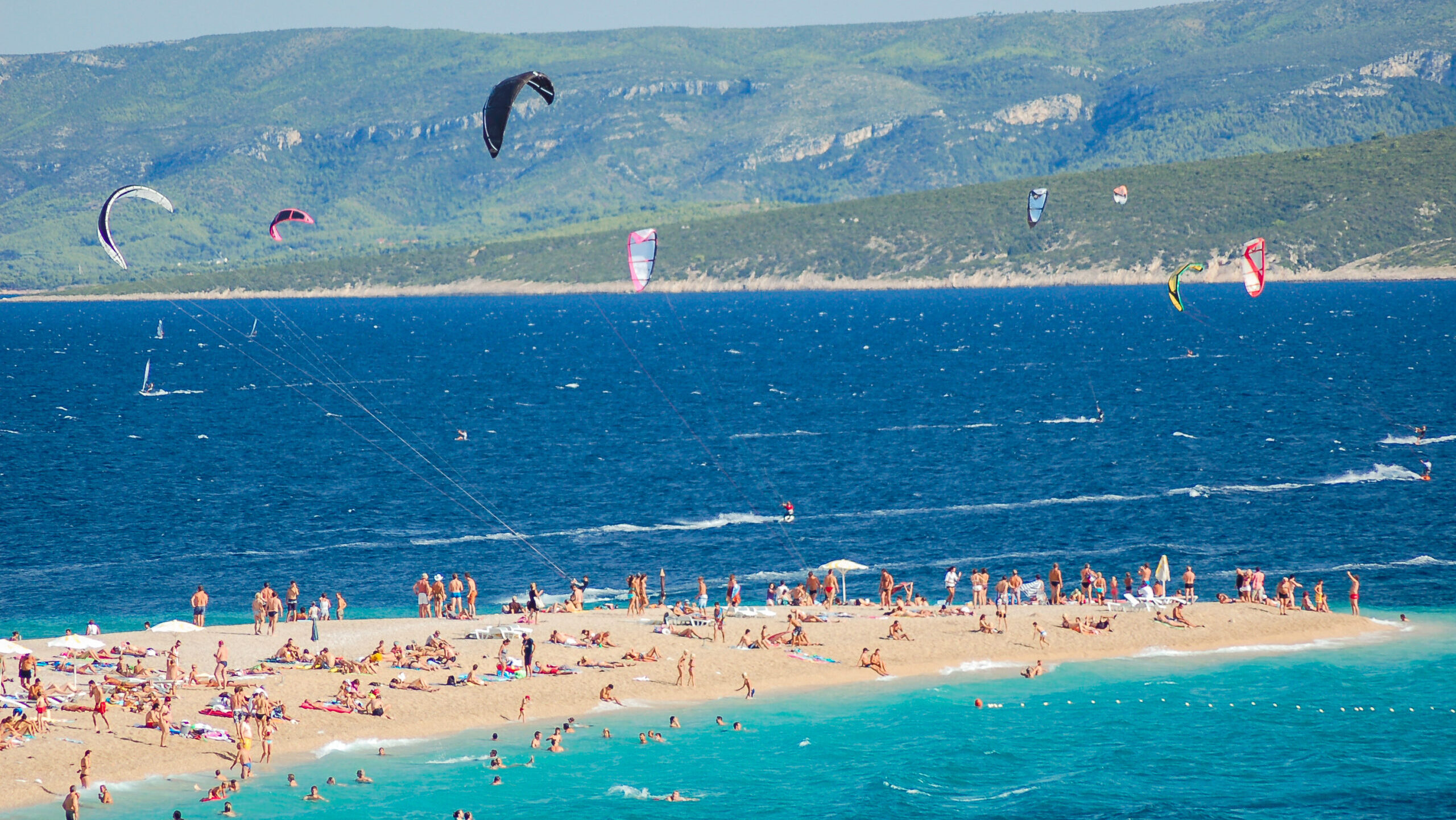Brač Island beach with people swimming, sunbathing and flying with parachutes high in the sky