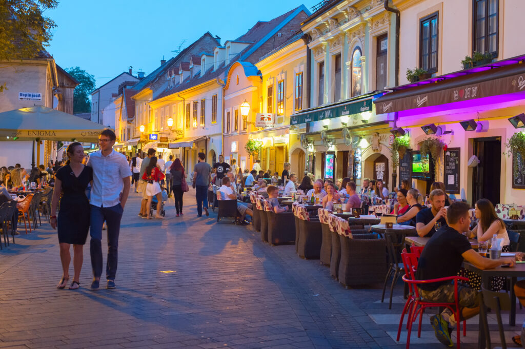 how safe is Croatia for travel - people sitting and eating at night on a busy street as a couple walk arm in arm
